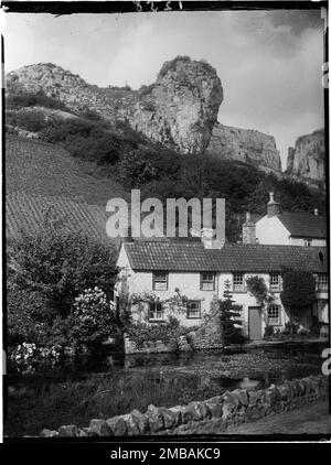 Mark Hole Cottage, The Cliffs, Cheddar, Sedgemoor, Somerset, 1907. Guardando attraverso il laghetto mulino vicino Cox's Mill verso Mark Hole Cottage e Lion Rock sulla collina sopra. La terra sul fianco della collina era sotto coltivazione, probabilmente per coltivazione di fragole. Le fragole sono ancora coltivate sulle pendici di Cheddar oggi e questa collina esposta a sud sarebbe stata l'ideale per coltivare la frutta morbida. I cottage in fondo alla collina sono contrassegnati sulle mappe come Mark Hole Cottage, ma nel 1985 sono stati inizialmente designati come un edificio elencato noto come Cheddar Pottery. Foto Stock