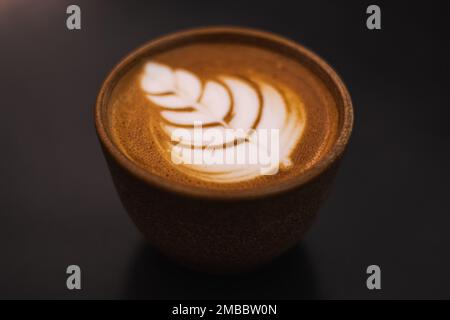 Primo piano Cappuccino in una tazza di ceramica con fiori o foglie disegnate sulla schiuma, sfondo nero, vista dall'alto Foto Stock
