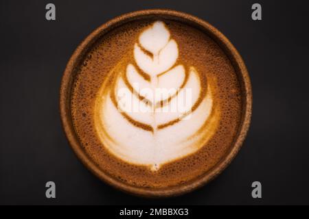 Primo piano Cappuccino in una tazza di ceramica con fiori o foglie disegnate sulla schiuma, sfondo nero, vista dall'alto Foto Stock