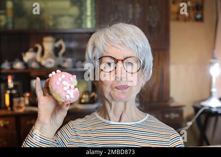 Donna anziana che mastica una ciambella Foto Stock