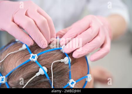 Il medico diagnostico rimuove gli elettrodi dalla testa del paziente anziano Foto Stock