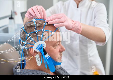 Il medico diagnostico collega gli elettrodi alla testa del paziente Foto Stock