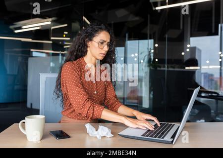 Giovane donna americana stanca che lavora su un computer portatile in ufficio. Si è ammalata, non si sente bene, straordinario. Foto Stock