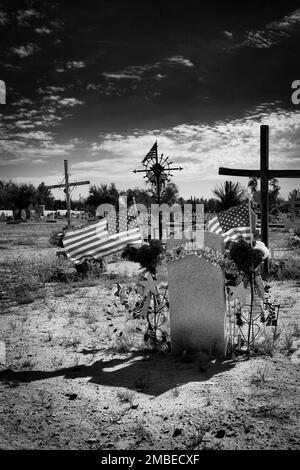 Le bandiere americane sventolano nella brezza sopra una tomba in un cimitero a Socorro, Texas. Foto Stock