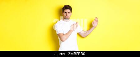 Uomo che mostra abilità kung-fu, arti marziali movimento ninja, in piedi in bianco t-shirt pronto a combattere, in piedi su sfondo giallo Foto Stock