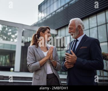 Uomo d'affari anziano e giovane donna che parlano di fretta di fronte all'edificio degli uffici Foto Stock