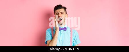 Immagine di un ragazzo stanco con bretelle a bocca aperta e occhi chiusi, in piedi sonnolenti, sensazione di stanchezza, in piedi su sfondo rosa Foto Stock