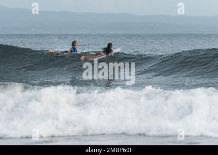 Surf a Keramas Beach, Bali, Indonesia, uomo e donna surf onde con un surf board, imparare surf a Kuta e Uluwatu Foto Stock