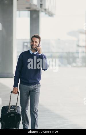 Fare affari mentre si è in viaggio. un bel giovane uomo d'affari in movimento con una valigia mentre usa il suo cellulare durante il giorno. Foto Stock