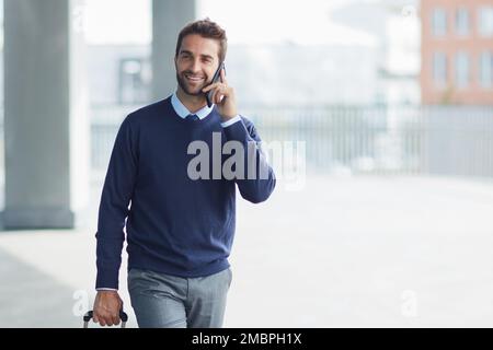 Im andare dopo i miei obiettivi di affari. un bel giovane uomo d'affari in movimento con una valigia mentre usa il suo cellulare durante il giorno. Foto Stock