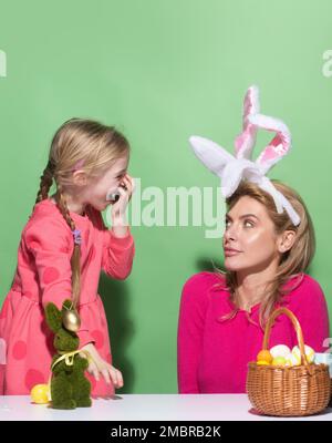 Estere per madre e figlia. Mamma con piccola ragazza carina si stanno preparando per Pasqua. Madre e figlia che indossano le orecchie conigliate stanno baciando. Banner di Pasqua Foto Stock