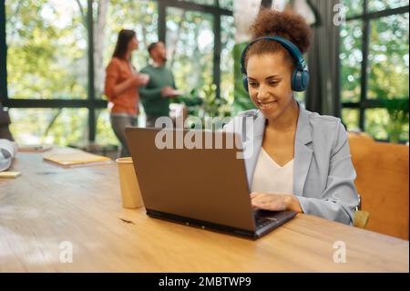 Giovane donna in viaggio d'affari con cuffie che utilizzano il notebook per il lavoro online Foto Stock
