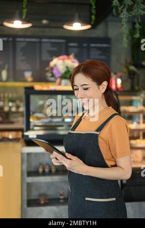 Ritratto di cameriera femminile in piedi in una caffetteria e utilizzando un tablet digitale per controllare le prenotazioni Foto Stock