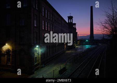 Luce rosa all'orizzonte all'alba su Salts Mills a Saltaire con luci all'aperto che si infrangono attraverso le ombre Foto Stock