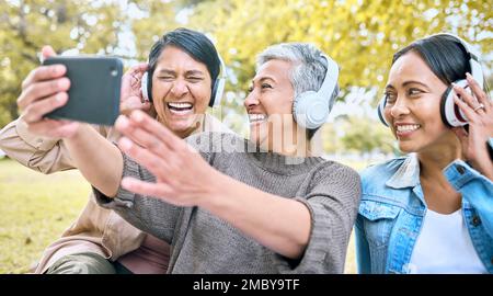 Donna anziana, amici e telefono ridendo con cuffie ascoltare musica o guardare film comici nel parco. Gruppo di donne anziane felici Foto Stock