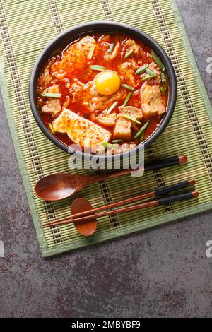 Sundubu jjigae è uno stufato coreano con tofu morbido, kimchi, pancia di maiale, cipolla e spezie primo piano sulla ciotola sul tavolo. Vista dall'alto verticale da circa Foto Stock