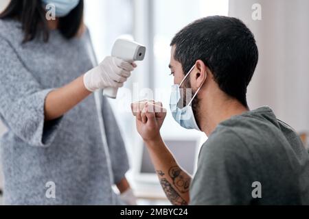 Alcuni sintomi non devono mai essere ignorati. una giovane donna che prende la temperatura dei mariti mentre si recupera da una malattia nel paese. Foto Stock