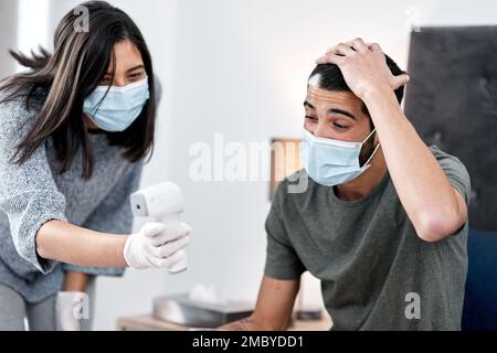 Non può essere così. una giovane donna che prende la temperatura dei mariti mentre si recupera da una malattia nel paese. Foto Stock
