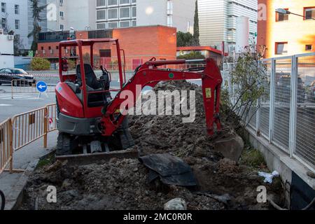 Il mini retroescavatore si è fermato, all'interno di un recinto recintato, sul cantiere, pronto per iniziare e lavorare con le pietre e la sabbia Foto Stock