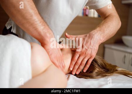 Vista ravvicinata delle mani del massaggiatore che dona un massaggio al collo e alla testa a una giovane donna Foto Stock