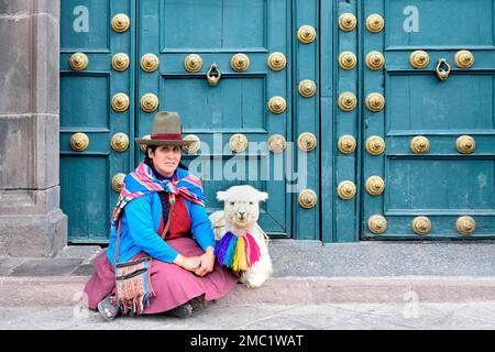 Donna nativa seduta con un lama di fronte alla porta d'ingresso della Basilica la Merced, Cusco, Perù Foto Stock