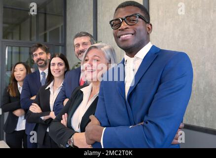 Un team diversificato di giovani felici in piedi insieme. Gruppo multietnico di colleghi in fila, braccia piegate e sorridenti. Concetti di lavoro di squadra Foto Stock