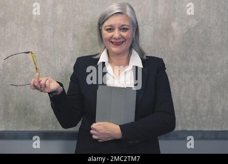 Donna anziana moderna in elegante vestiera con tablet digitale isolato sul grigio. Ritratto di una donna matura che lavora in ufficio utilizzando la tecnologia online per fare Foto Stock