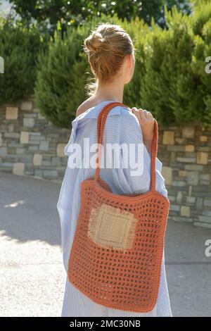 Giovane donna che indossa una grande borsa tote arancione a uncinetto fatta a mano nella località turistica, stile di moda estiva, vacanza rilassante Foto Stock
