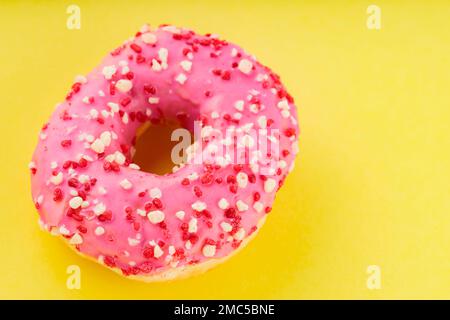 Ciambella rosa dolce con spolverini multicolore su fondo giallo. Dessert dolce colorato Foto Stock
