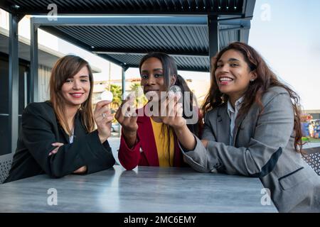 Tre attraenti commercianti di sesso femminile sorridono mentre tiene in mano le monete di bitcoins in una riunione di affari Foto Stock