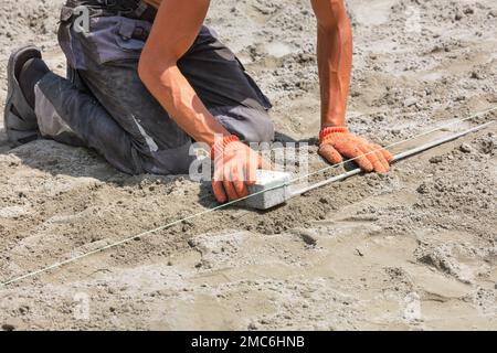 Un lavoratore che si schiantava verso il basso stabilisce il giusto livello con il filo di nylon prima di posare le lastre di pavimentazione in una giornata estiva di sole. Spazio di copia. Foto Stock