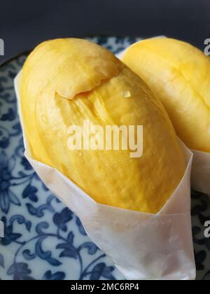 Primo piano due di carne Durian di colore giallo dorato avvolta con carta bianca sul piatto antico di colore blu, forma e forma naturali, fondo scuro, iso Foto Stock