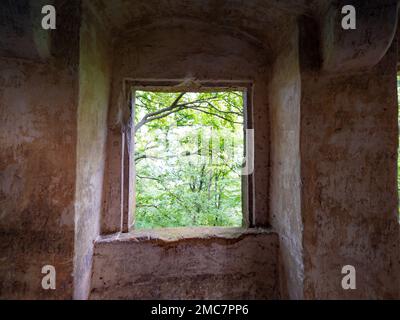 Casa di pietra con vetrata di pietra. Casa in pietra abbandonata con finestra vuota si affaccia su una foresta nebbiosa. Foto Stock