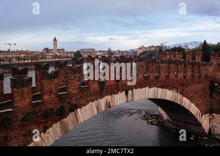 Verona, gennaio 2023. Una figura solitaria sotto un ombrello attraversa il ponte Scaligero sull'Adige in un suggestivo paesaggio urbano. Foto Stock