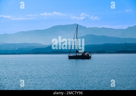 Una barca a vela si ancora in una baia vicino alla costa, le colline in lontananza sono avvolte nella nebbia. Foto Stock