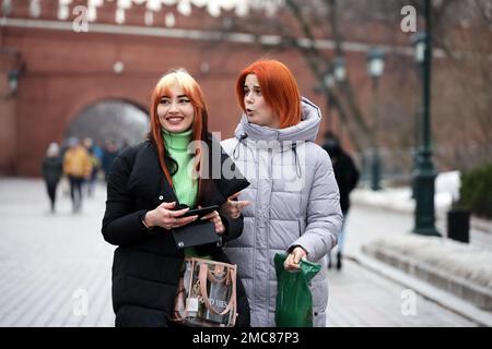 Due donne felici con i capelli tinti che indossano i vestiti di inverno ripartiscono le loro impressioni mentre camminano insieme sulla strada della città Foto Stock