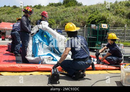 Vigili del fuoco e ingegneri con installazioni del corpo marino Pacific Fire and Emergency Services costruiscono una linea di decontaminazione durante un esercizio di formazione sui materiali pericolosi a Camp Hansen, Okinawa, Giappone, 27 giugno 2022. La formazione HAZMAT ha incluso più vittime simulate in un ambiente pericoloso, neutralizzando al contempo l'area contaminata. MCIPAC F&ES è un reparto antincendio regionale che gestisce otto stazioni antincendio in tutto il Giappone e fornisce servizi alle installazioni, tra cui antincendio, soccorso tecnico, materiali pericolosi, pronto soccorso, protezione antincendio e prevenzione. Foto Stock