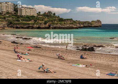 I turisti prendono il sole sulla sabbia della spiaggia di Ostende nella città di Castro Urdiales in provincia di Cantabria, Spagna, Europa Foto Stock