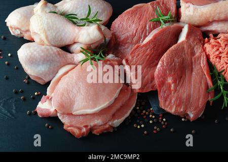 Vari tipi di carne fresca: Maiale, manzo, tacchino e pollo su un tavolo nero di legno Foto Stock