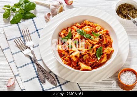 tortellini in salsa di pomodoro di manzo macinato in ciotola bianca su tavola di legno bianco con forchette Foto Stock