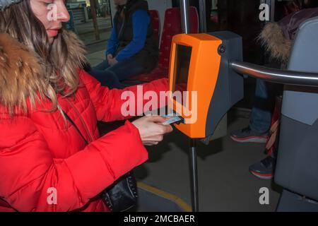 Giovane donna alla moda che utilizza una macchina punzonatrice per biglietti nei trasporti pubblici. La ragazza prende a pugno il biglietto. Foto Stock