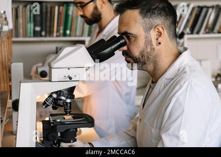 Visualizzazione dello scienziato il campione attraverso il microscopio durante l'esperimento in laboratorio Foto Stock