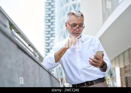 Uomo d'affari anziano che tiene il telefono cellulare utilizzando il cellulare all'aperto. Foto Stock