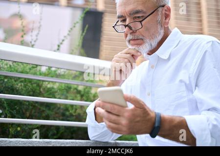 Uomo d'affari anziano che tiene il telefono cellulare utilizzando il cellulare all'aperto. Foto Stock