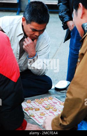 Un uomo asiatico adulto contempla la sua prossima mossa durante una partita di xianggi con i suoi amici in un parco cittadino Foto Stock