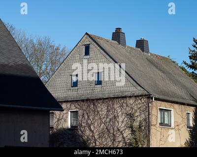 Materiale in amianto sulla parete esterna e sul tetto di una casa residenziale. I fogli di cemento pericolosi sull'edificio sono pericolosi. Foto Stock