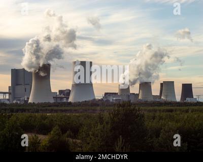 Fumo emesso da una centrale alimentata a lignite. Gas a effetto serra che inquinano l'aria in una zona rurale. Torri di raffreddamento con ciminiere nel paesaggio. Foto Stock