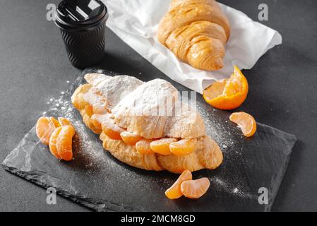 Panino di croissant dolce con zucchero a velo su fondo scuro. Concetto di panificazione e panetteria Foto Stock