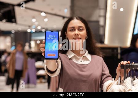 Cyber monday. Ritratto sfocato di sorridente giovane donna caucasica mostra smartphone con acquisti in negozio online sullo schermo. Concetto di shoppin online Foto Stock