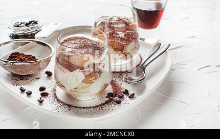Tiramisù tradizionale dessert italiano in una tazza di vetro. Tiramisù fatto in casa in una tazza di vetro, processo di cottura graduale. Tradizionale dessert italiano non cotto Foto Stock